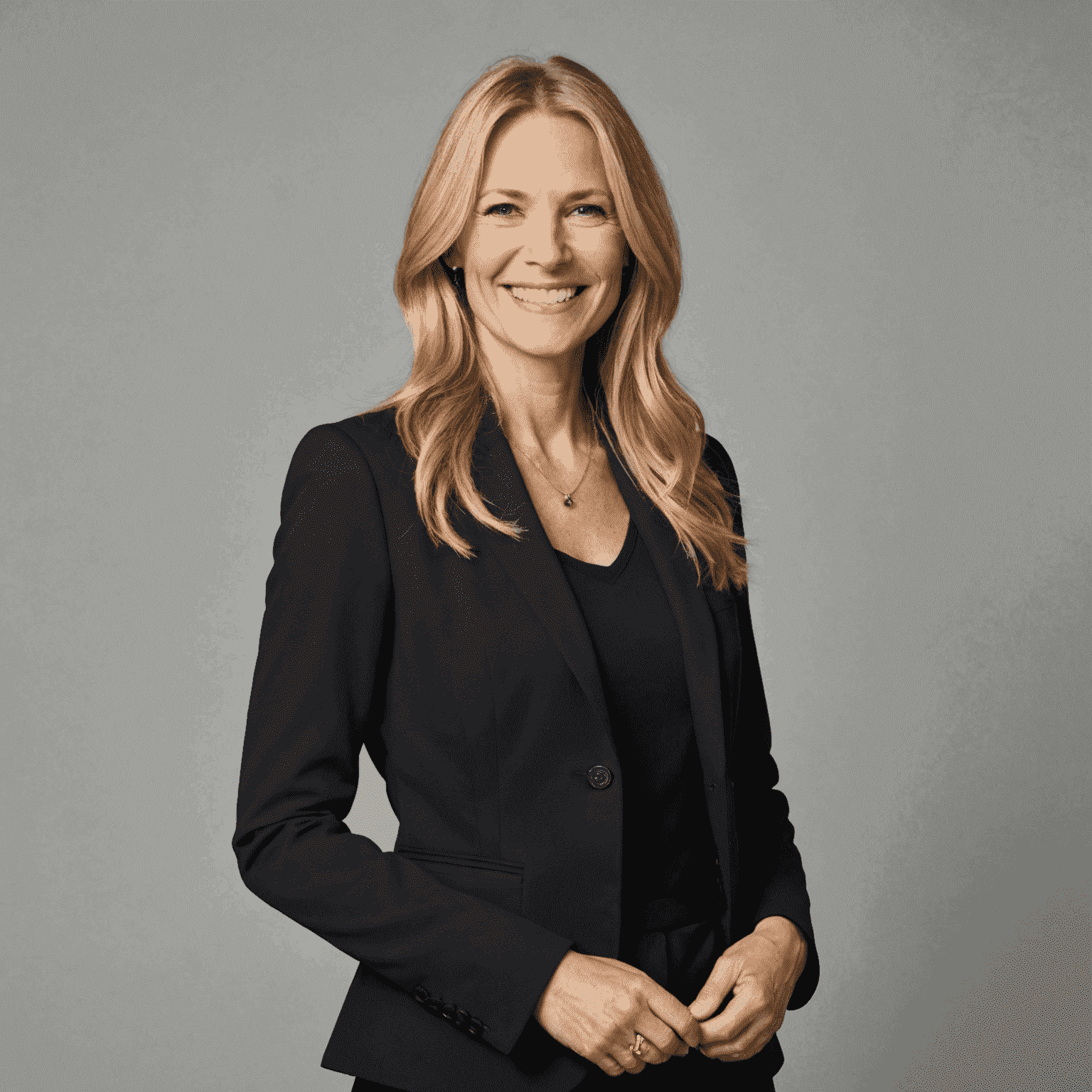 Portrait of a smiling woman in her 40s with long blonde hair, wearing a black blazer